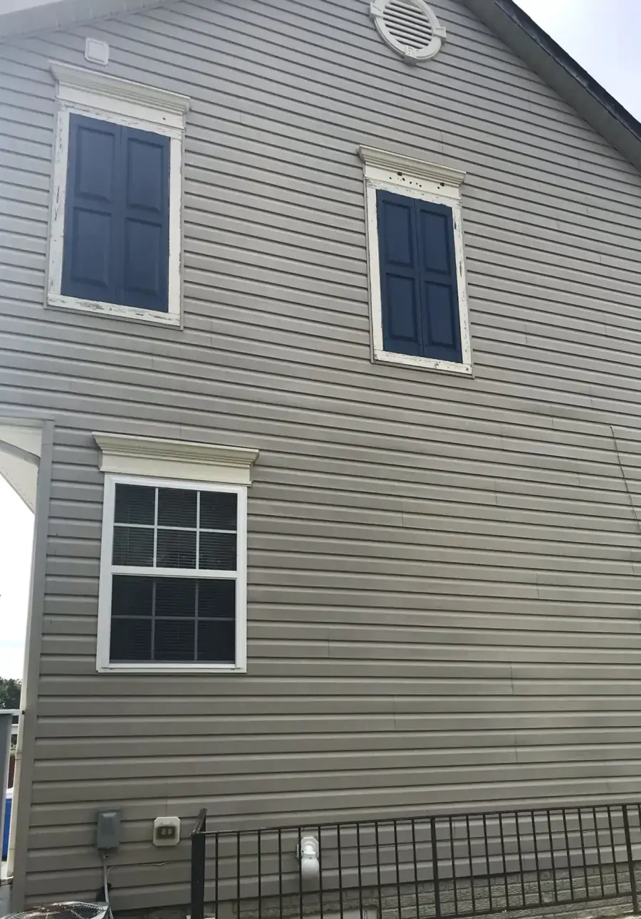 The same vinyl siding gable wall after a soft wash, even grey, shutters and trim clean