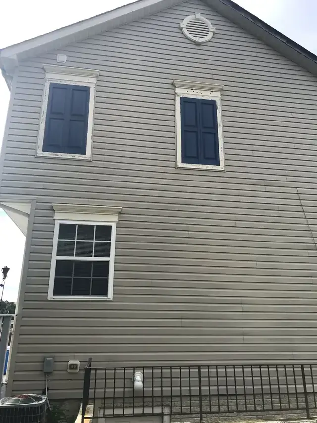 Grey vinyl siding on a two-storey gable wall after a soft wash, navy shutters and white trim clean