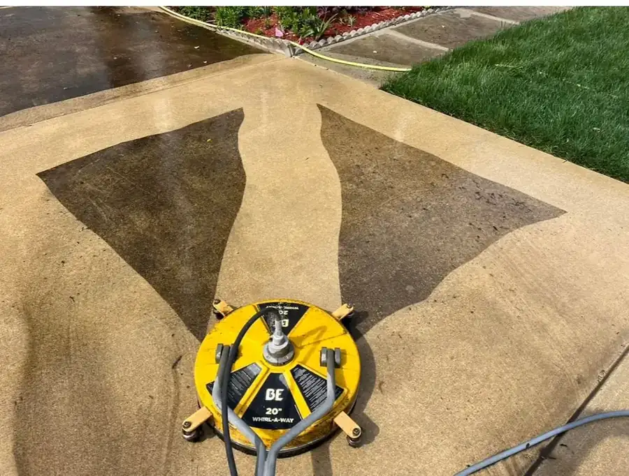 Yellow surface cleaner on a driveway, two pale clean lanes cut through dark weathered concrete